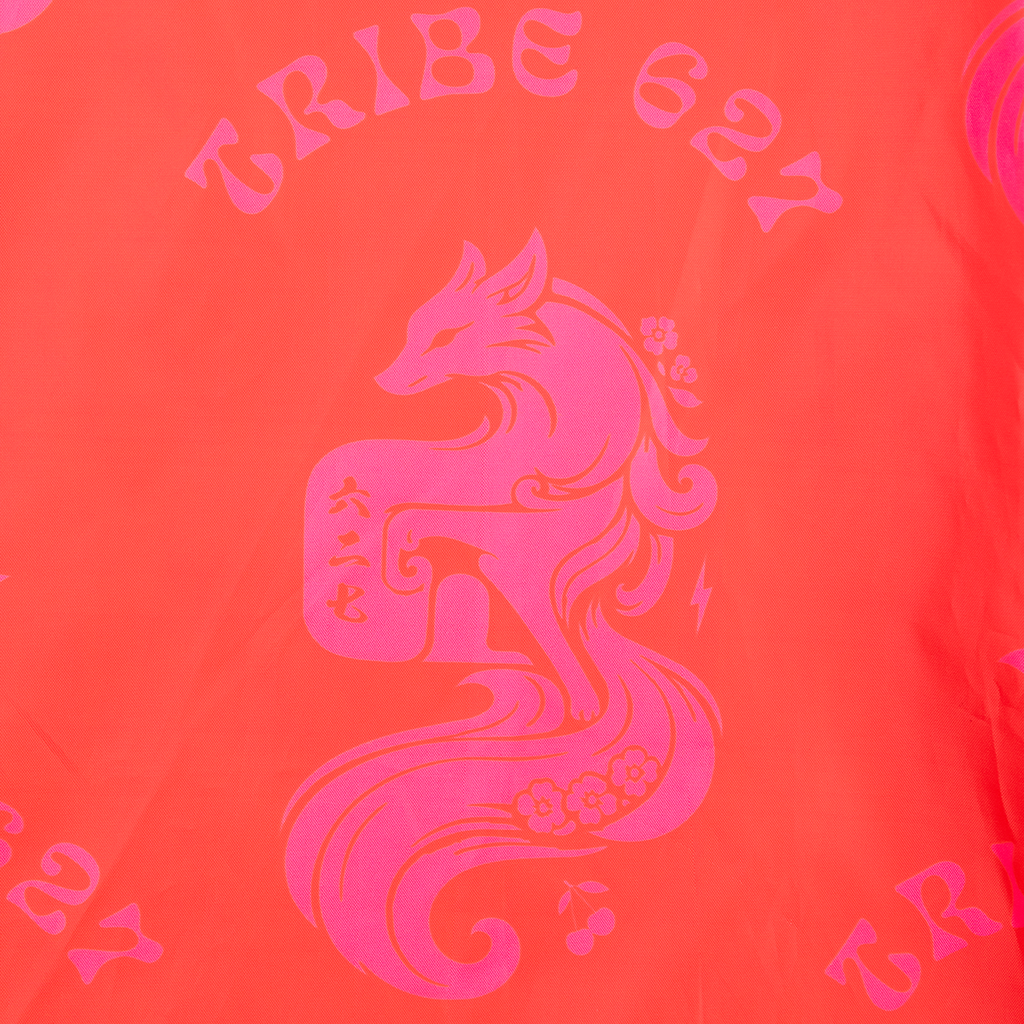 A close-up of a bright coral-orange fabric with a large hot pink graphic of a stylized fox and the words "TRIBE 627" printed above it.