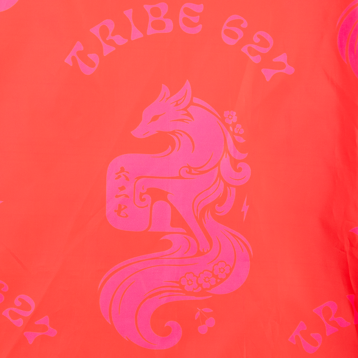 A close-up of a bright coral-orange fabric with a large hot pink graphic of a stylized fox and the words "TRIBE 627" printed above it.