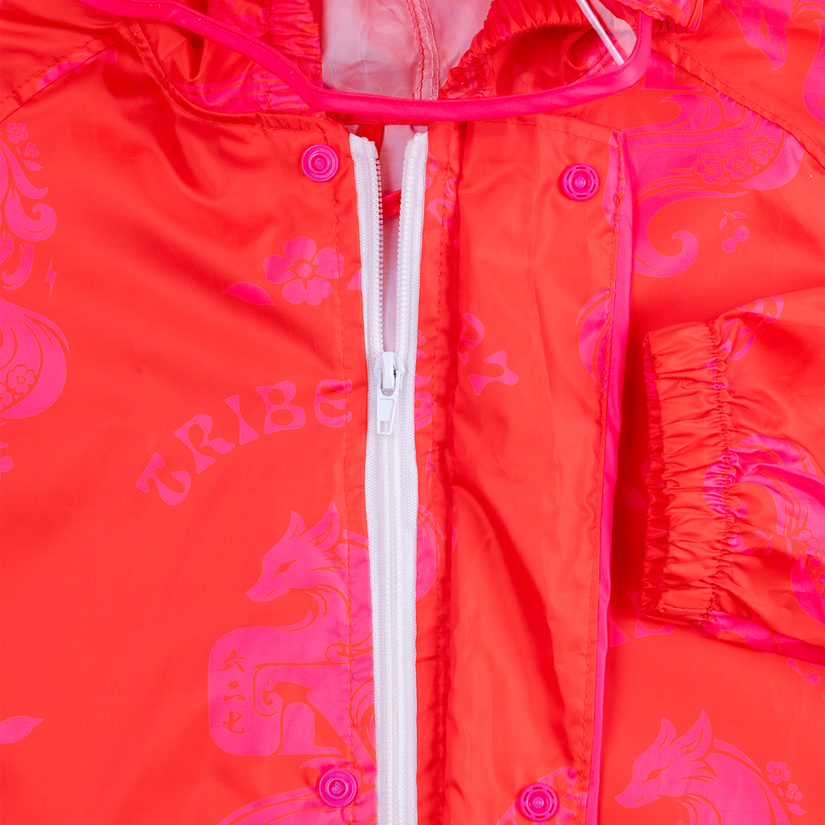 Close-up of a bright neon pink hooded jacket with a white front zipper, pink snap buttons, and a tonal pink graphic pattern featuring foxes and the word TRIBE.