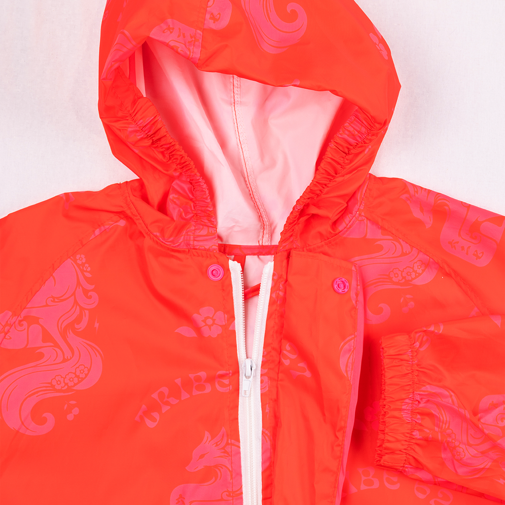 A close-up of a bright orange hooded jacket with a pink abstract pattern, featuring a white zipper and pink buttons.